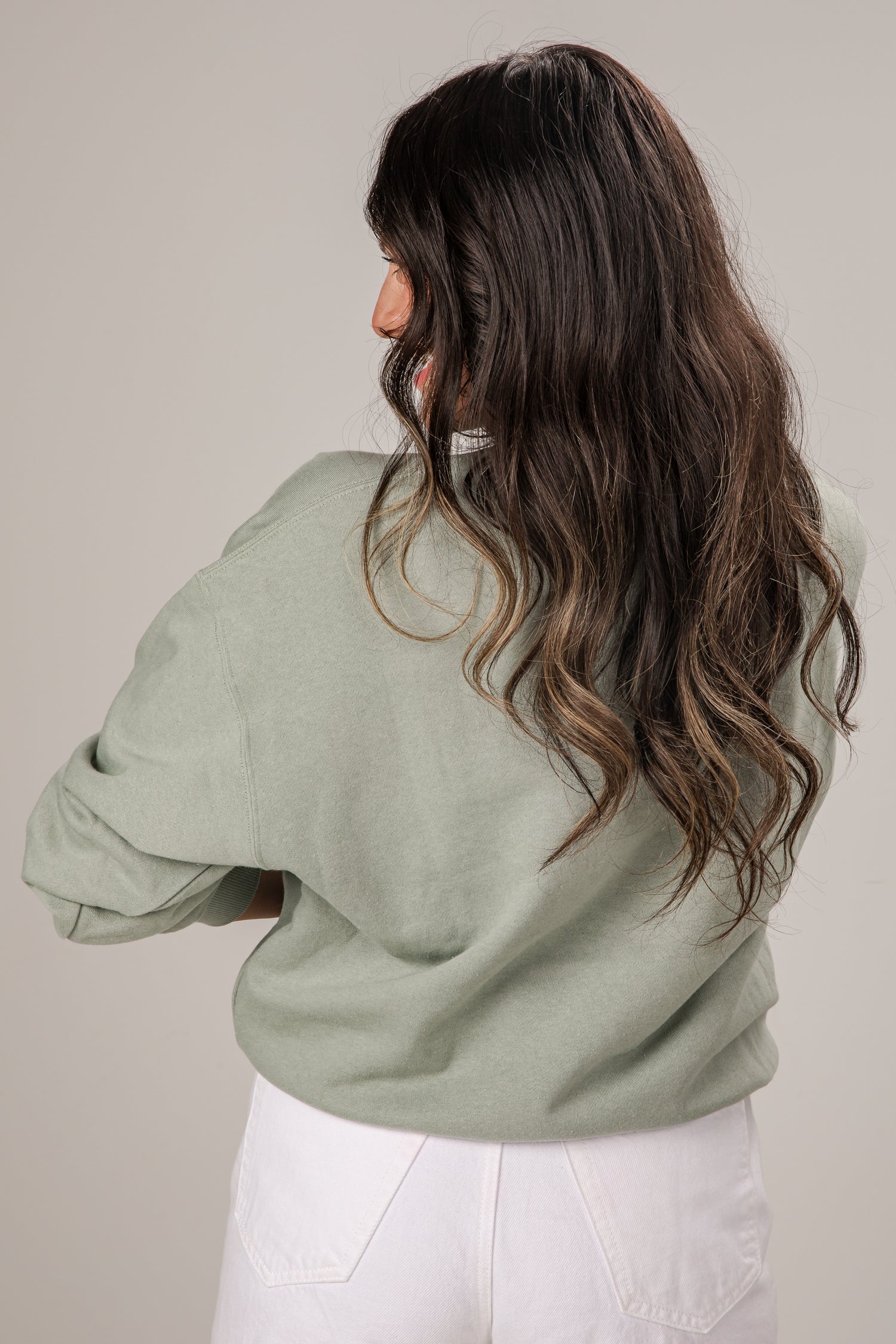 Woman wearing a light green sweater and white pants against a plain background