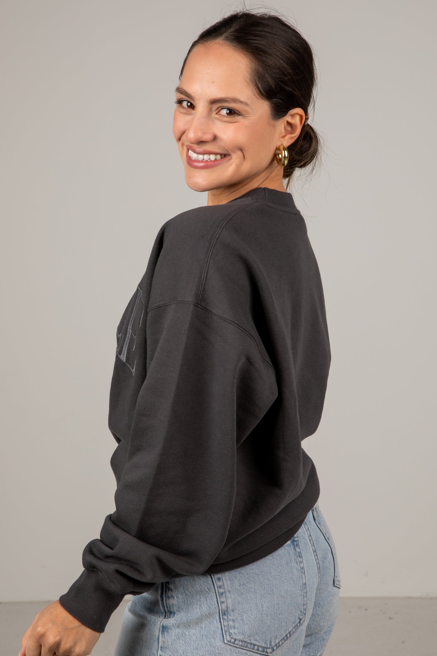 Woman wearing a dark gray sweatshirt and light blue jeans against a plain background