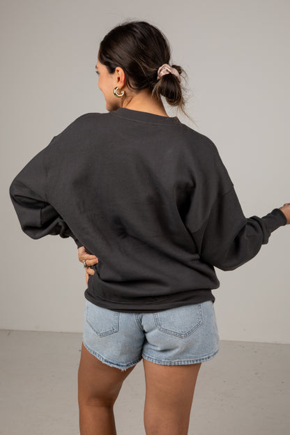Person wearing a black sweatshirt and denim shorts against a plain background