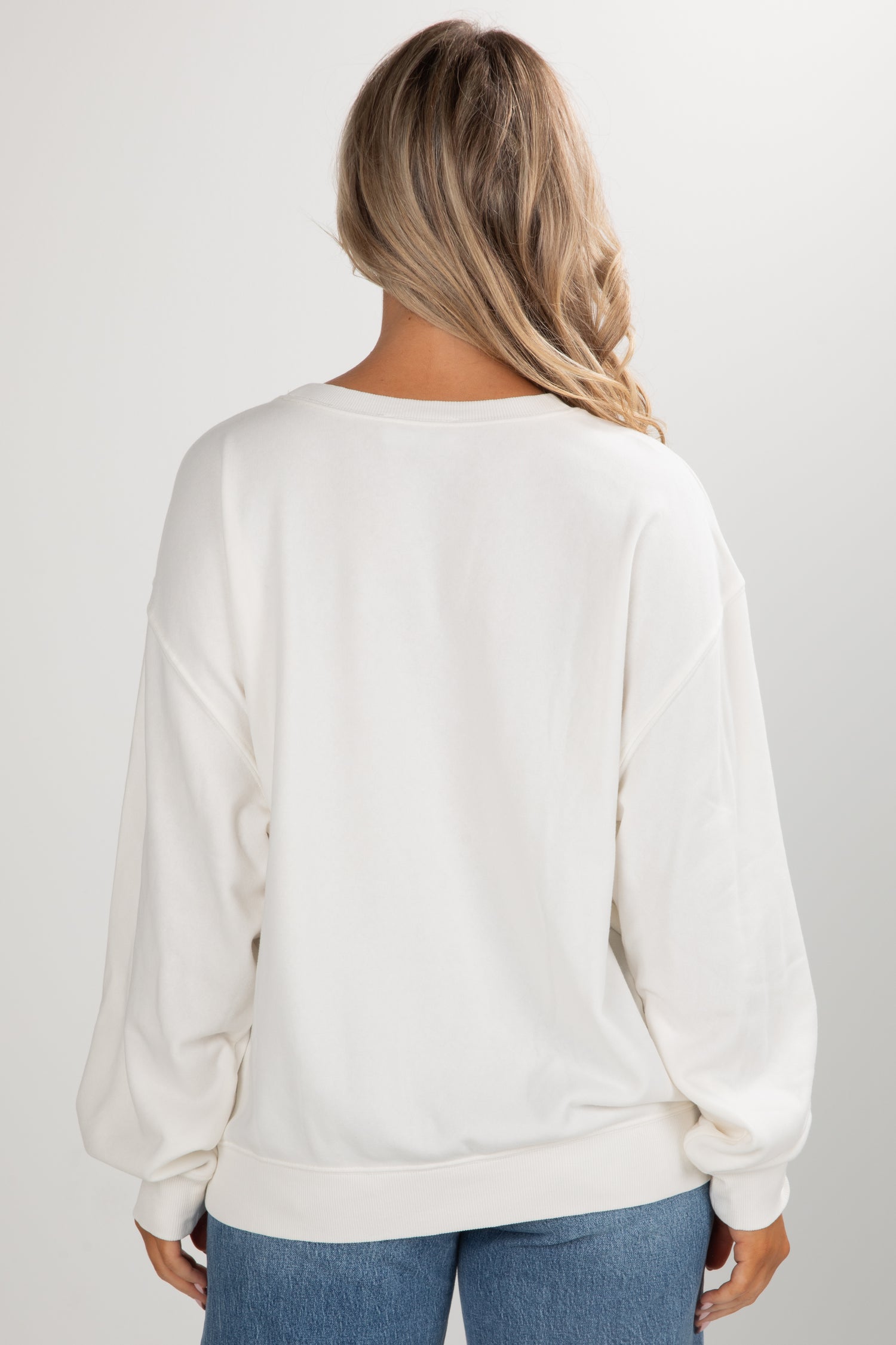 Person wearing a white sweater and blue jeans on a plain background