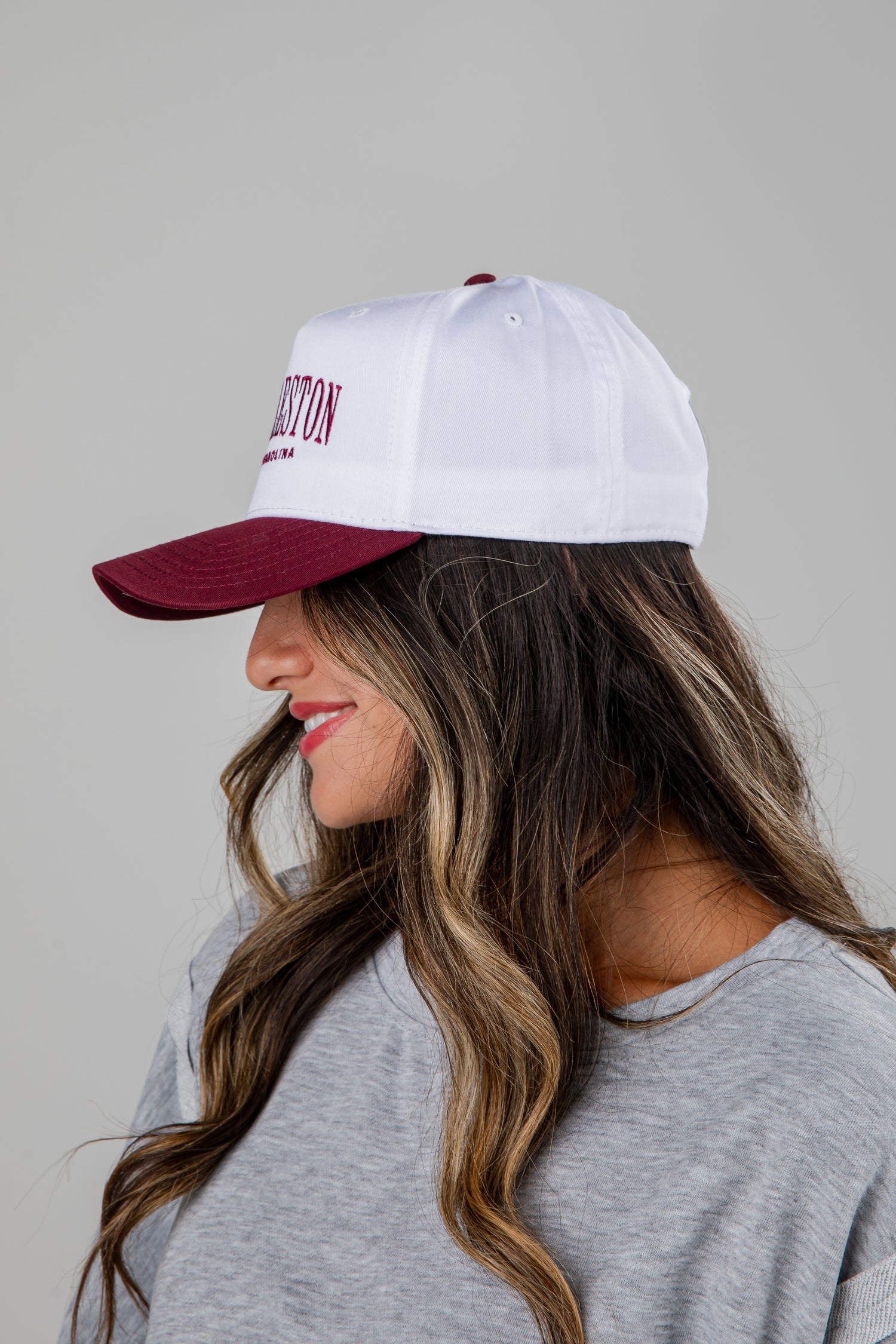 Woman wearing a white cap with red brim and text, against a plain background
