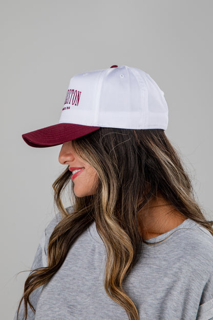Woman wearing a white cap with red brim and text, against a plain background