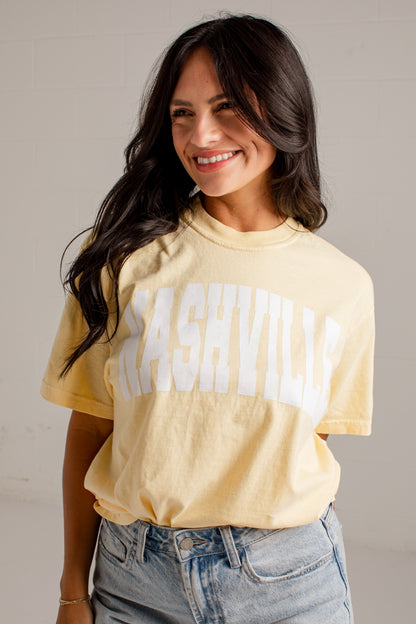 A woman wearing a pale yellow graphic t-shirt with &
