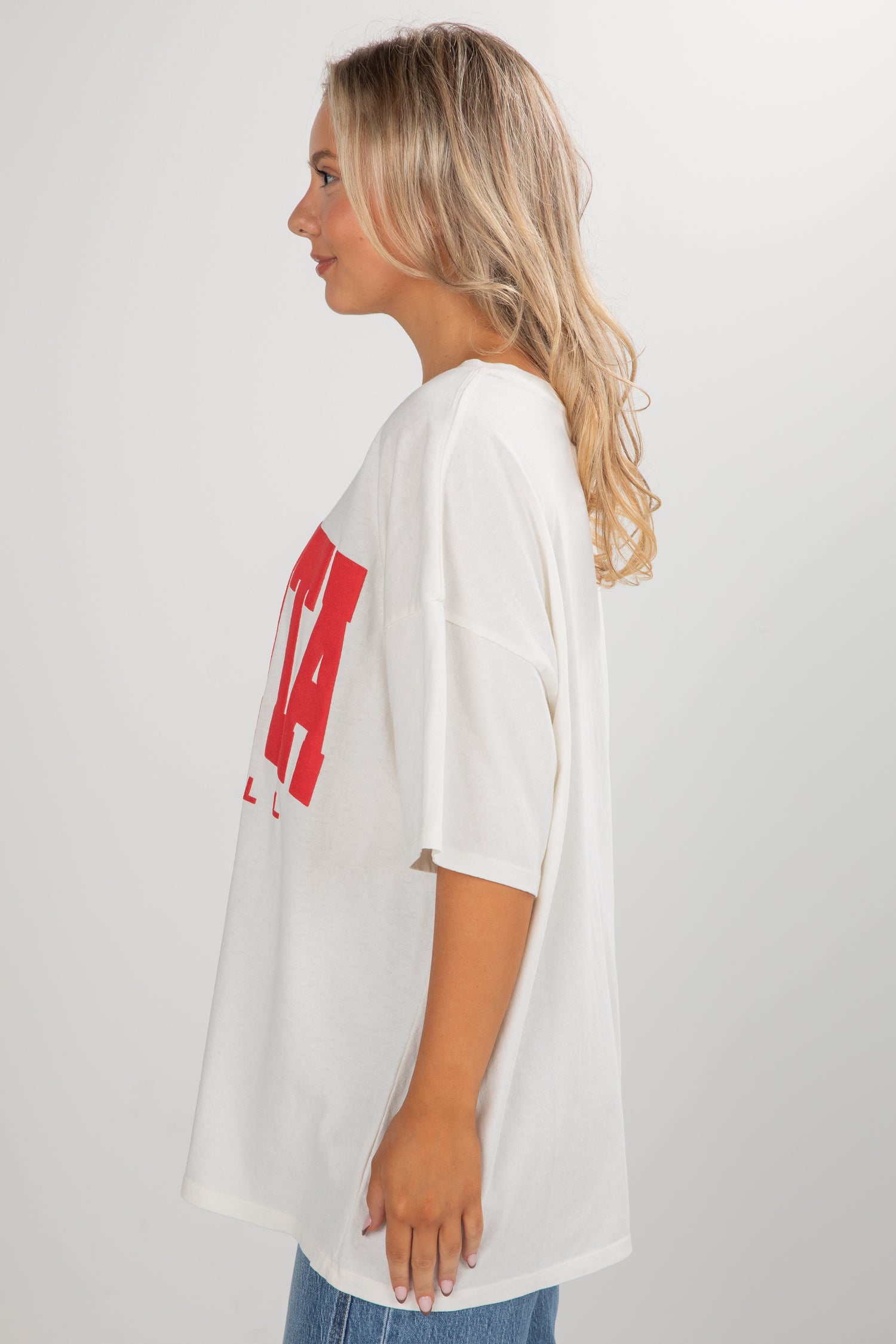 Woman wearing a white oversized t-shirt with red text on a plain background