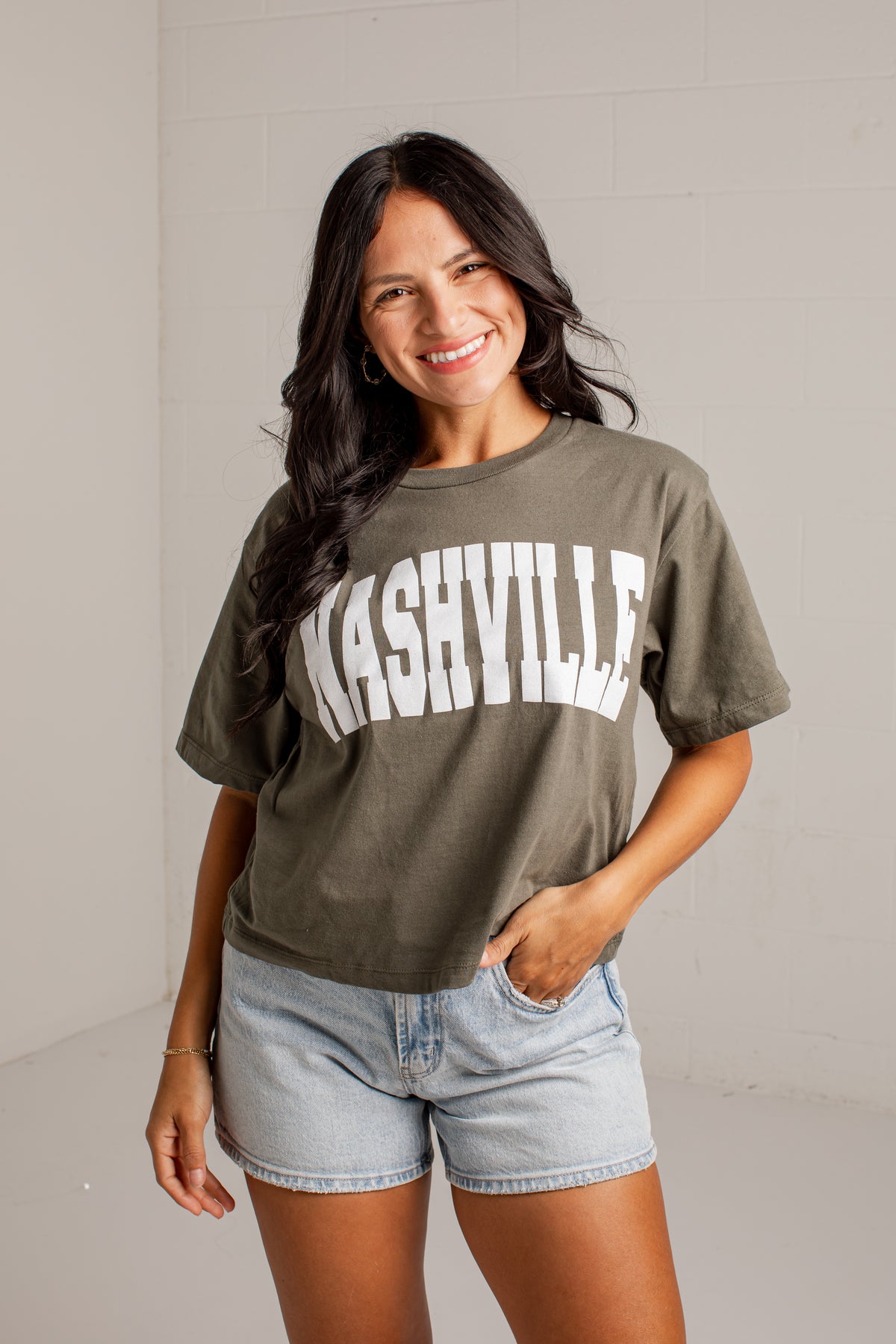A woman wearing an olive green graphic t-shirt with &