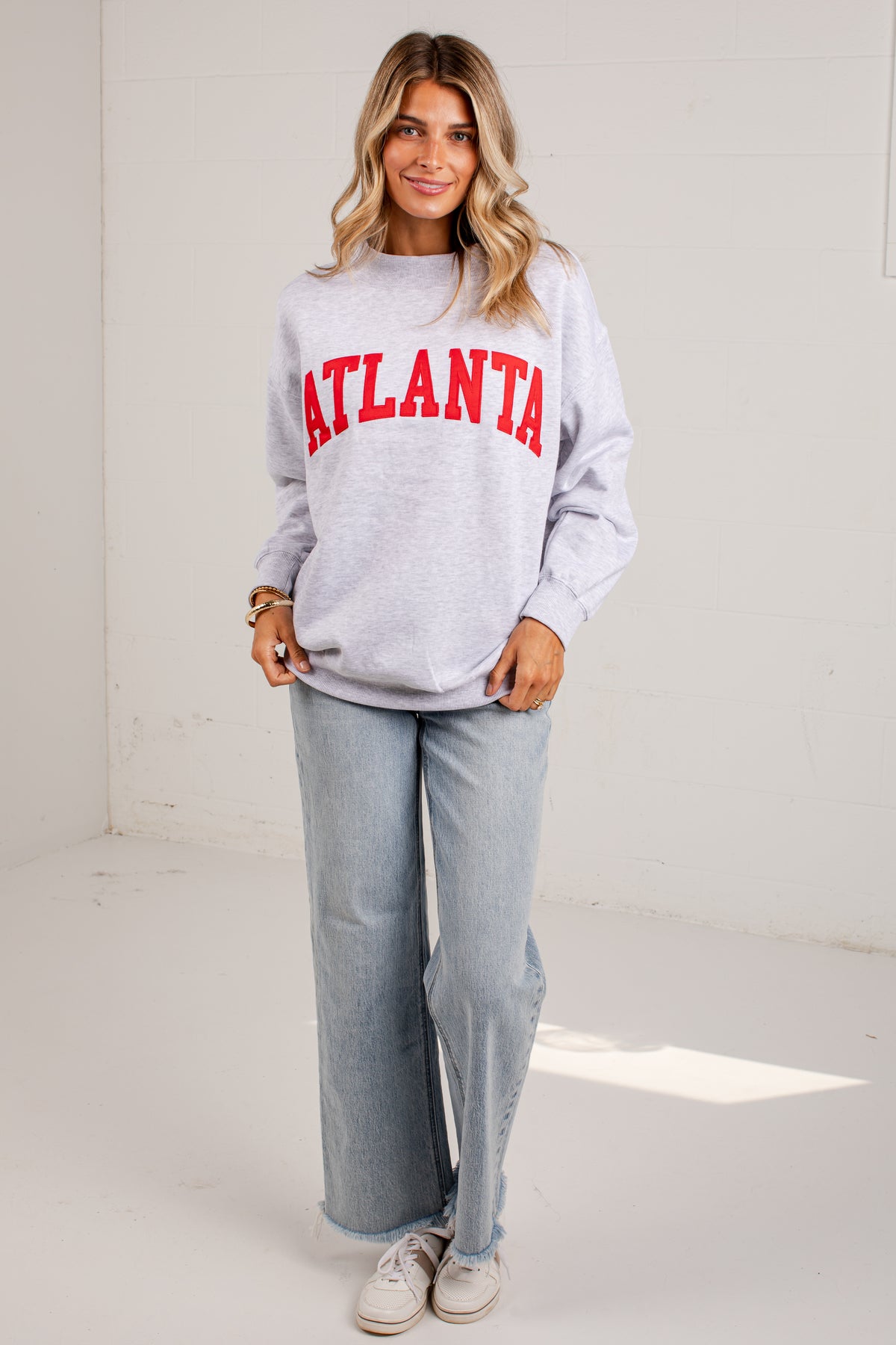 A woman modeling a light gray crewneck sweatshirt with &