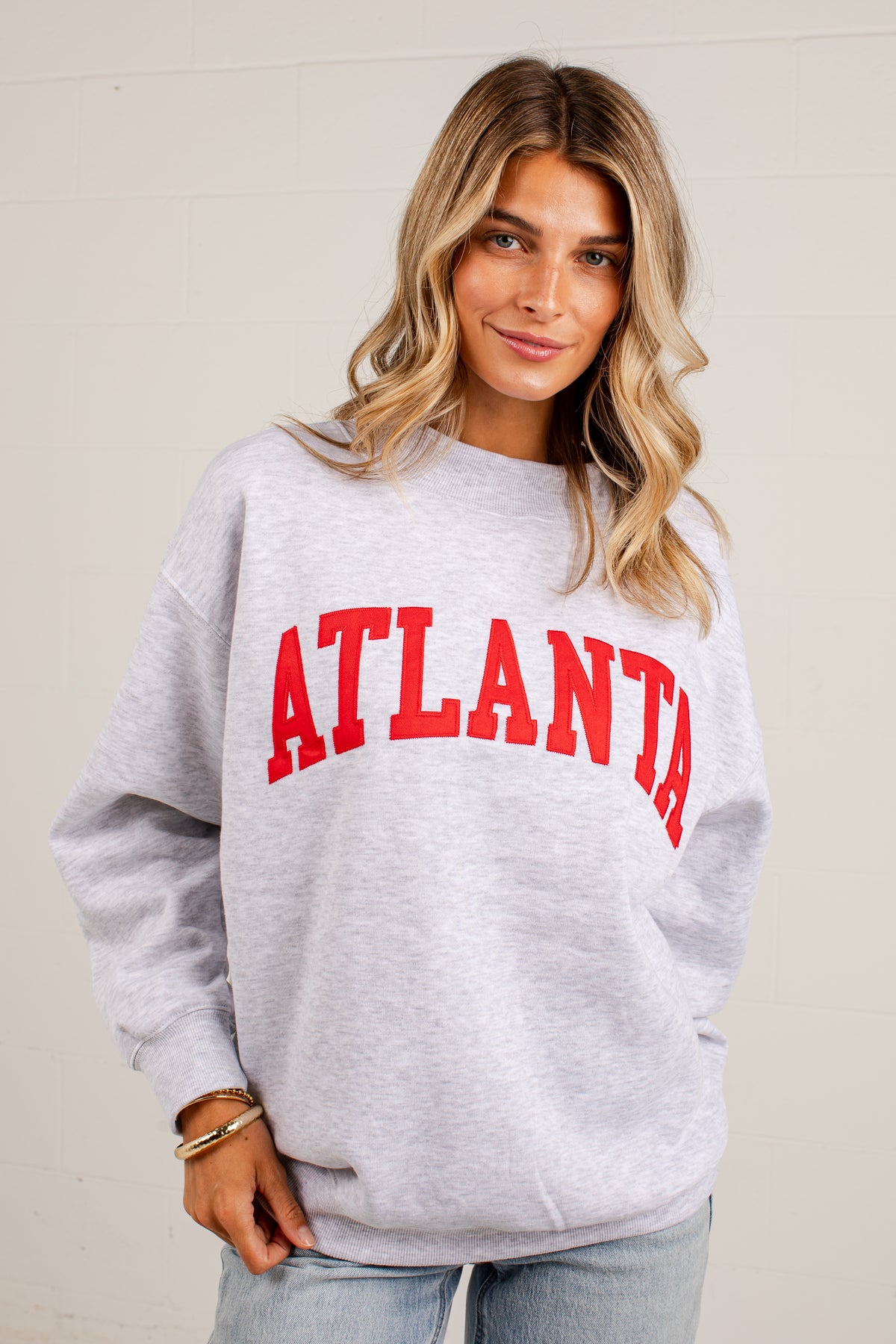 A woman wearing a light heather gray crewneck sweatshirt with &