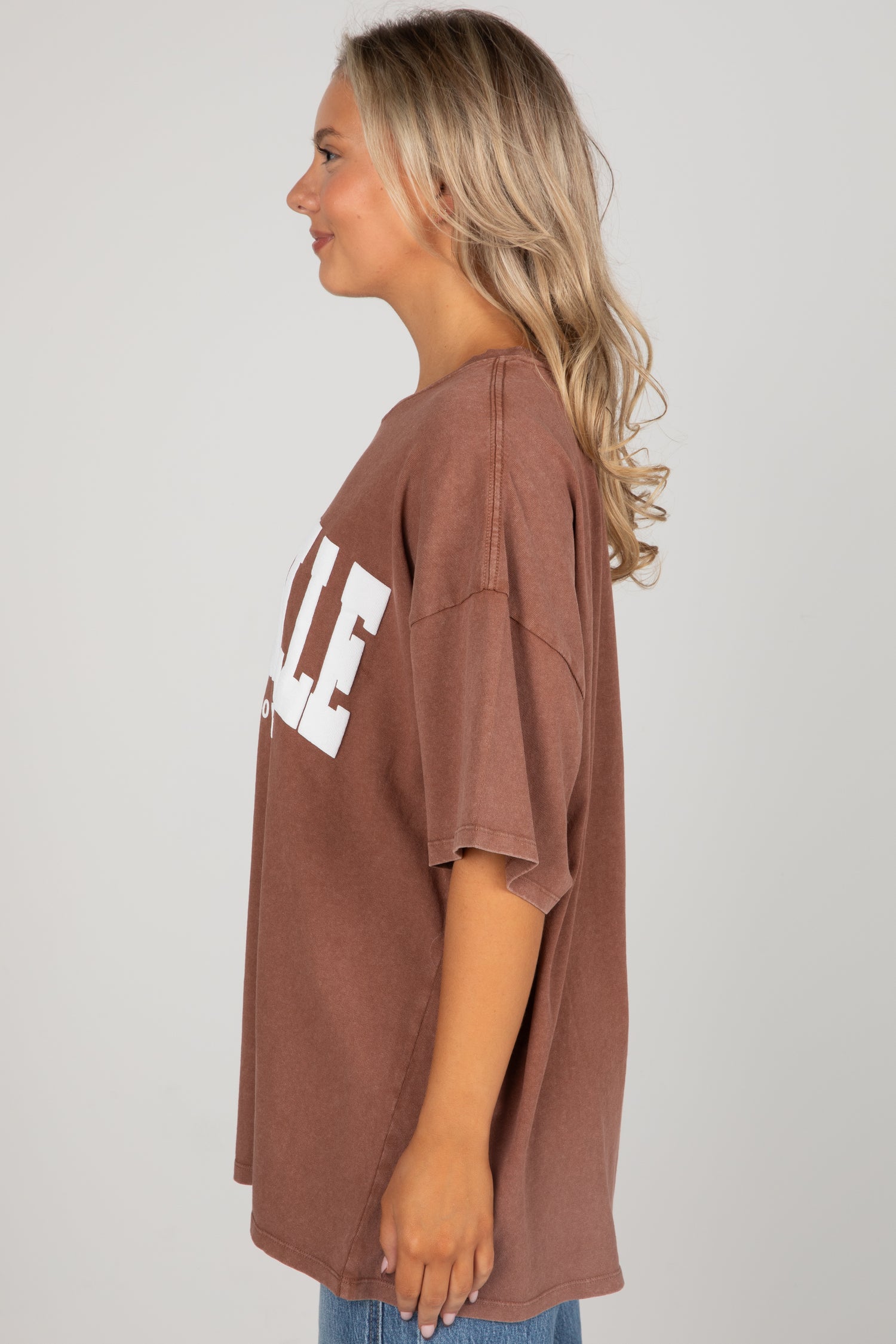 Woman wearing a brown oversized t-shirt with white text on a plain background