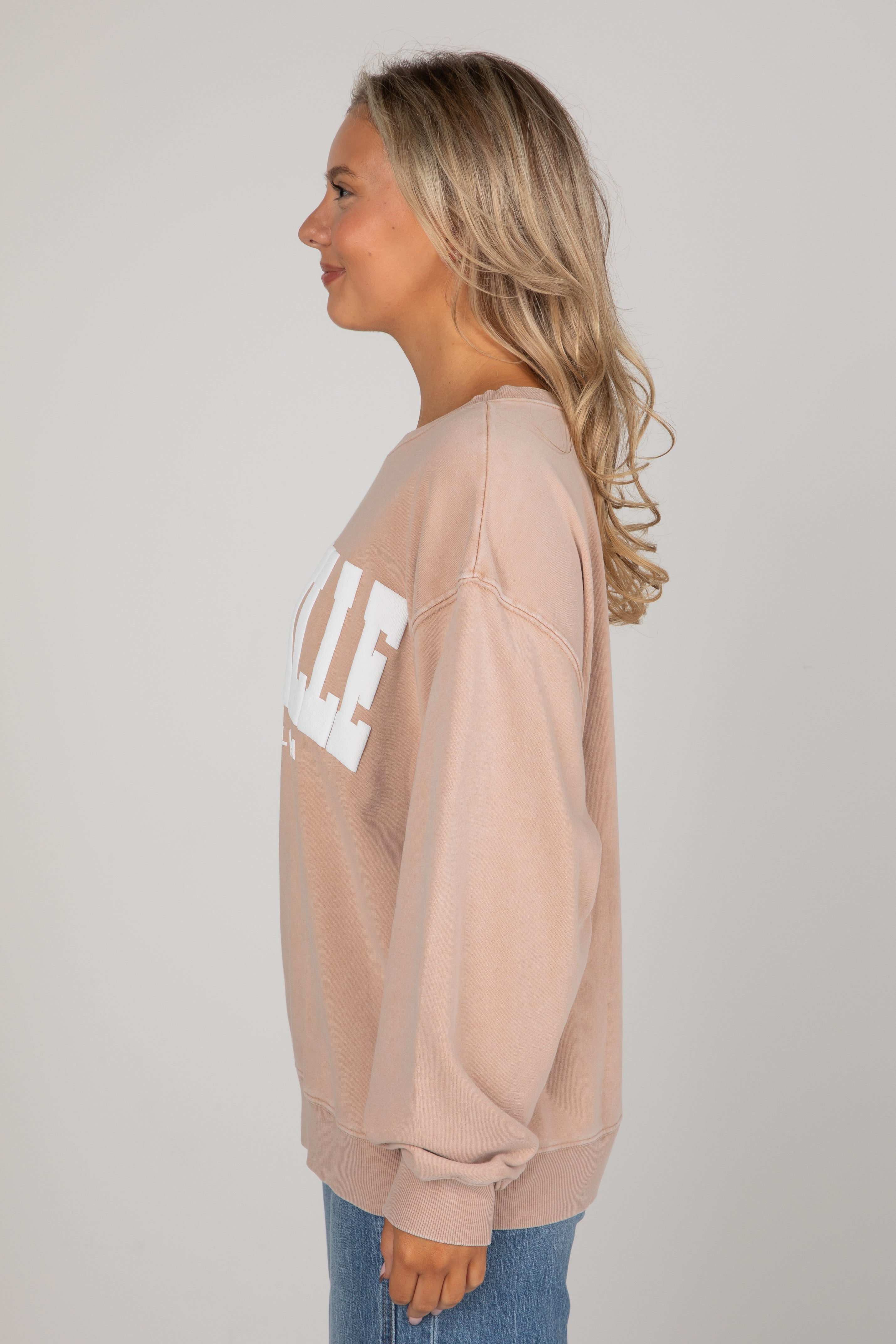 Woman wearing a beige sweatshirt with text on a plain background