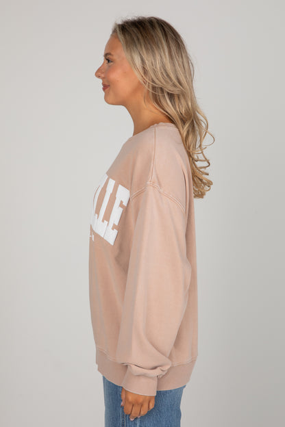 Woman wearing a beige sweatshirt with text on a plain background