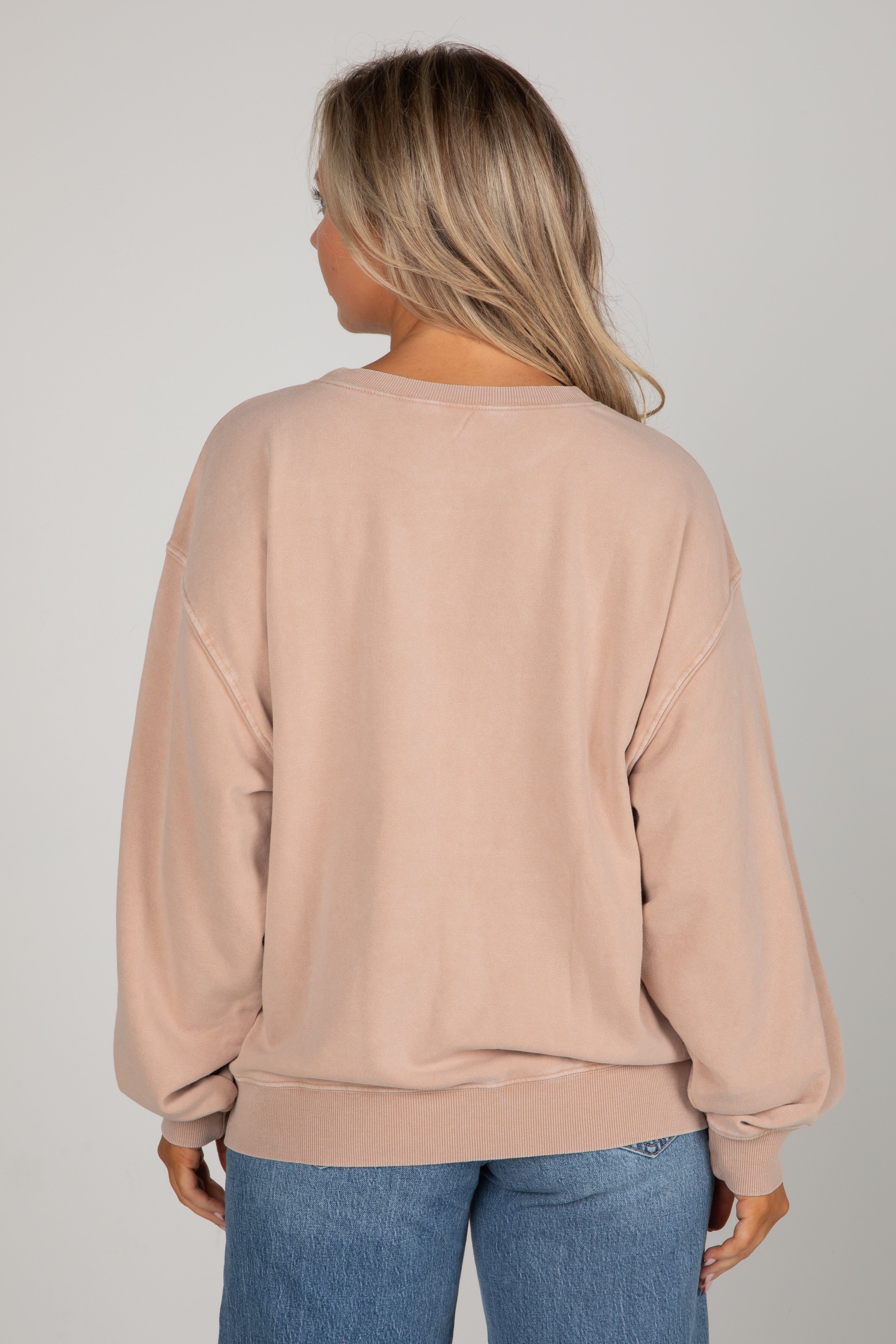 Person wearing a beige sweatshirt and blue jeans on a plain background