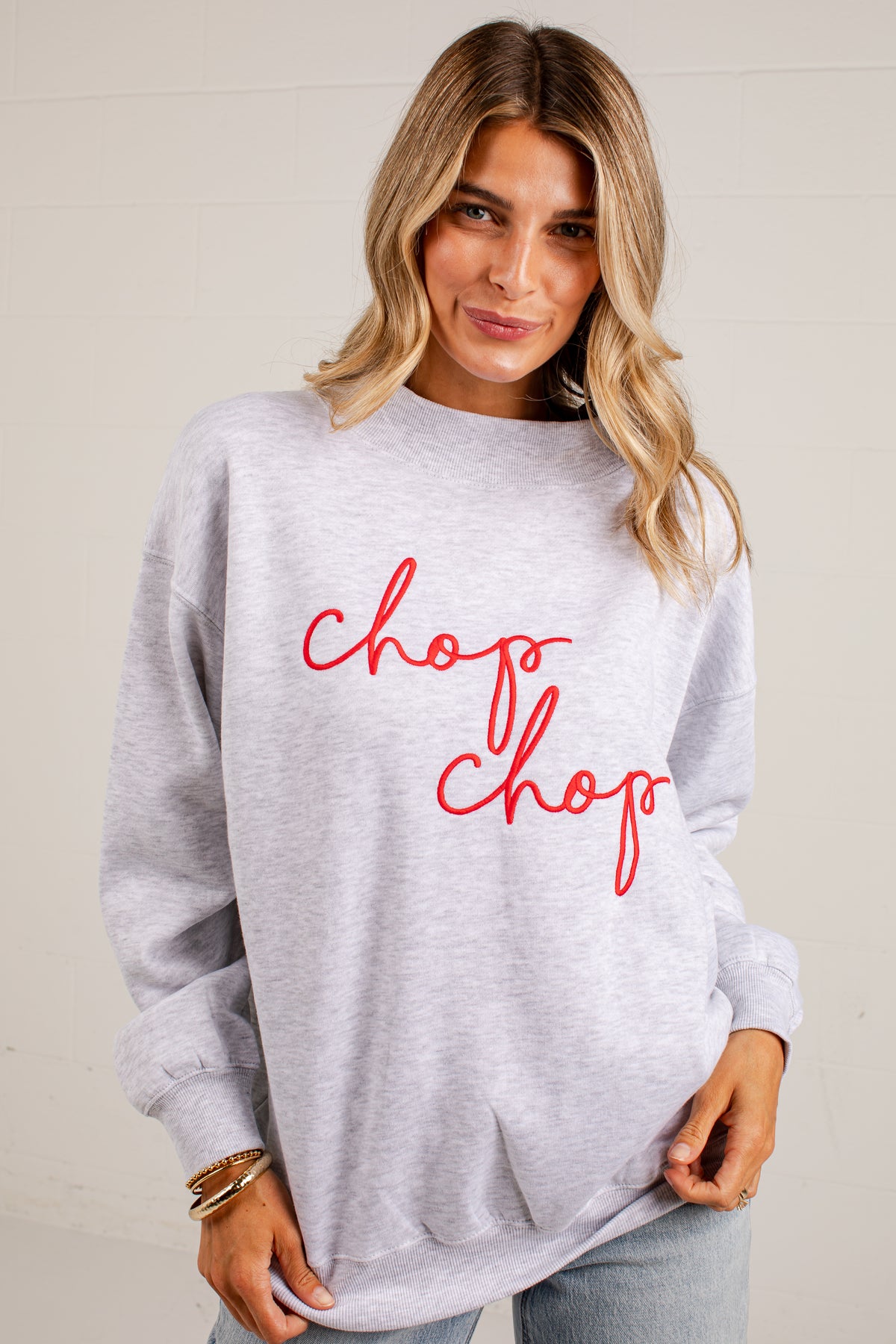 A woman wearing a light heather gray crewneck sweatshirt with the words &