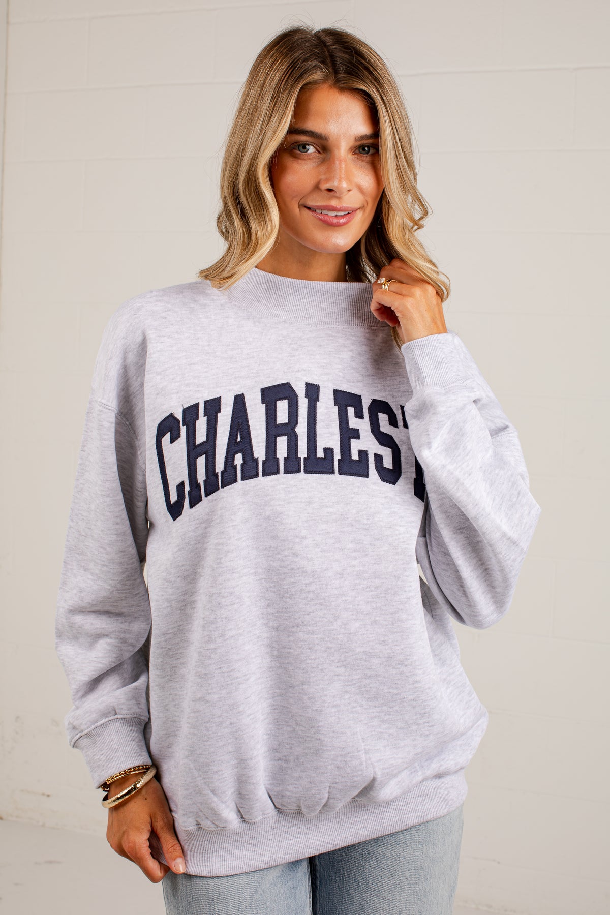 A woman wearing a light heather gray crewneck sweatshirt with &
