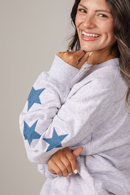 Woman wearing a gray sweater with blue star patterns on a plain background