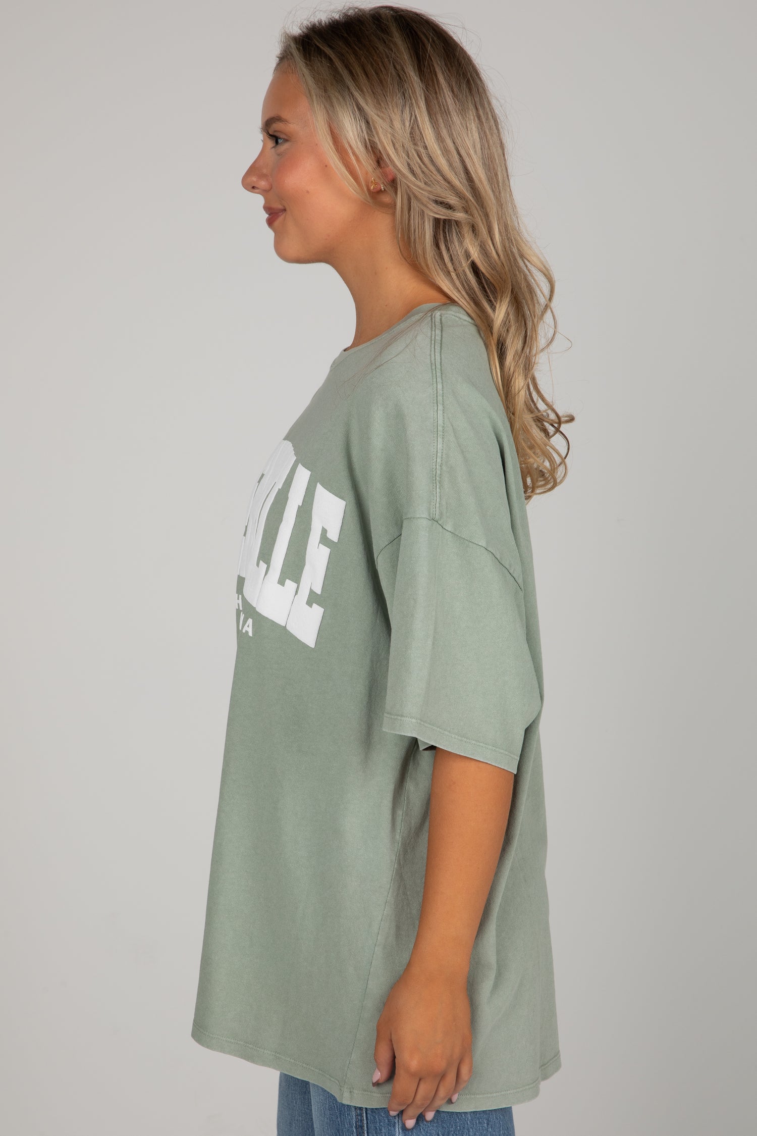 Woman wearing a green oversized t-shirt with text on a plain background