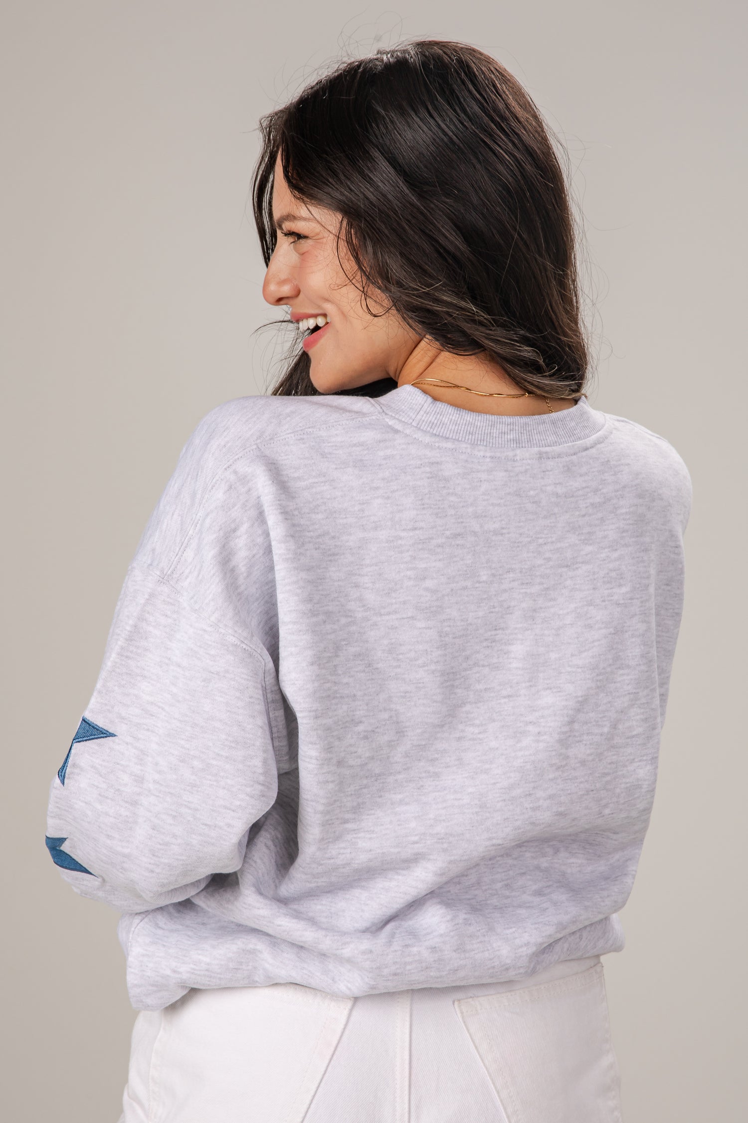Woman wearing a light gray sweatshirt with rolled-up sleeves on a plain background