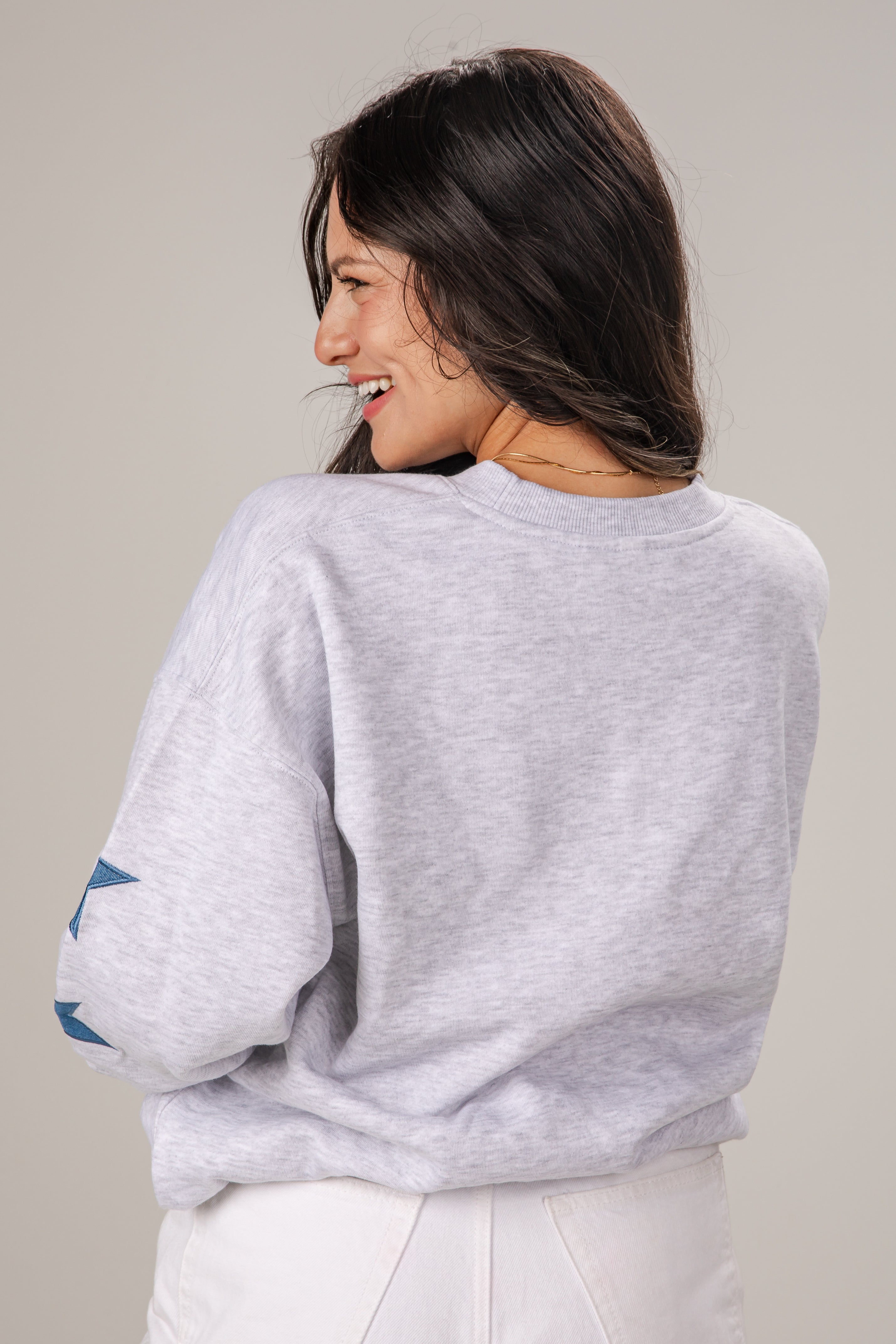 Woman wearing a light gray sweatshirt with rolled-up sleeves on a plain background