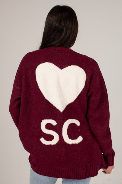 A woman viewed from behind wearing a maroon knit sweater with a large white heart and the letters &