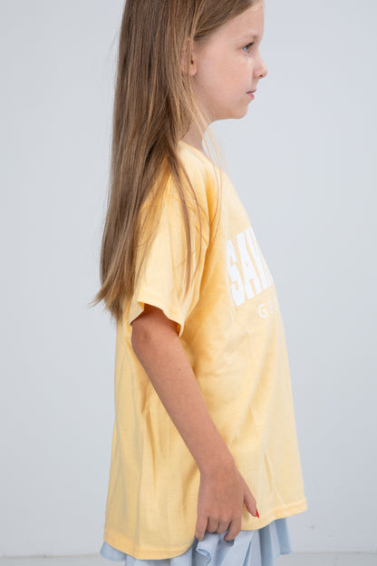 Young girl wearing a yellow t-shirt with text on a plain background