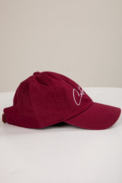 Maroon baseball cap with a logo on a white surface