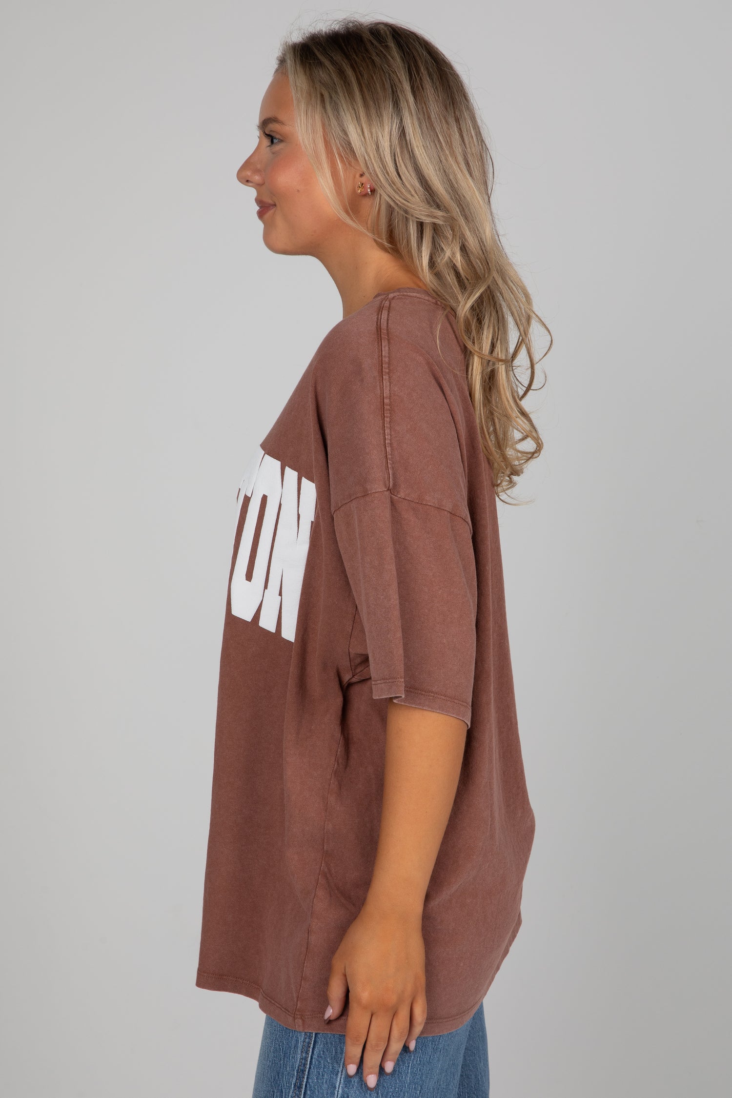 Woman wearing a brown oversized t-shirt with text on a plain background