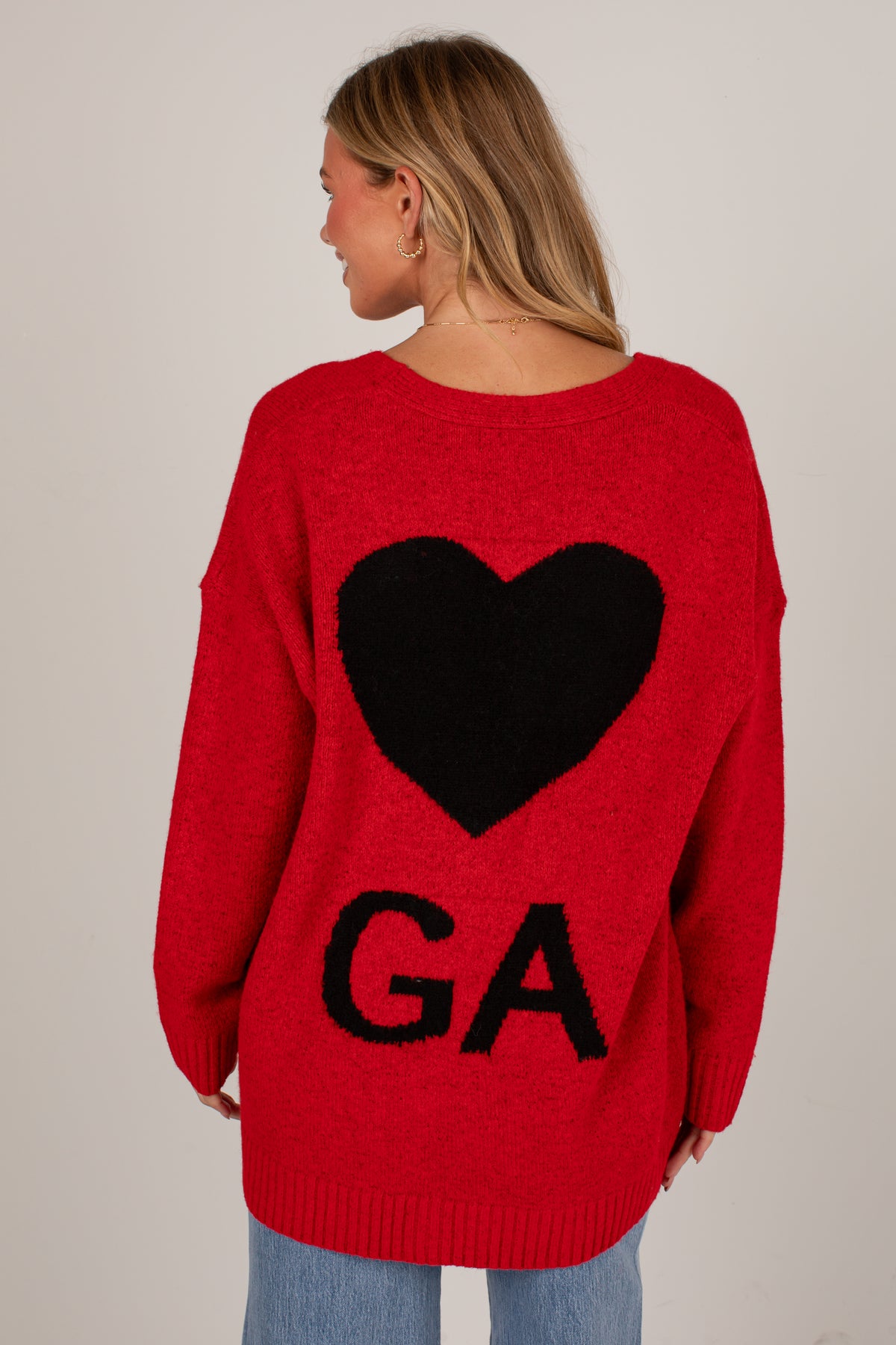 A woman shown from the back wearing a bright red knit sweater with a large black heart and the letters &