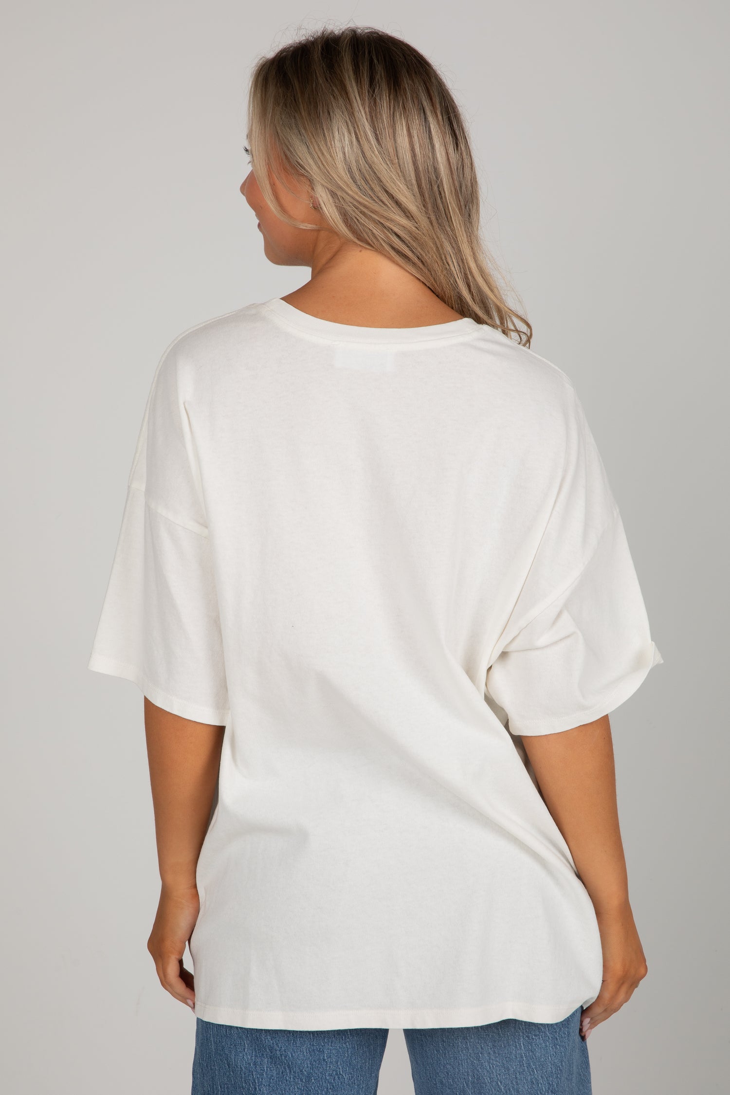 Person wearing a white oversized t-shirt and blue jeans on a gray background