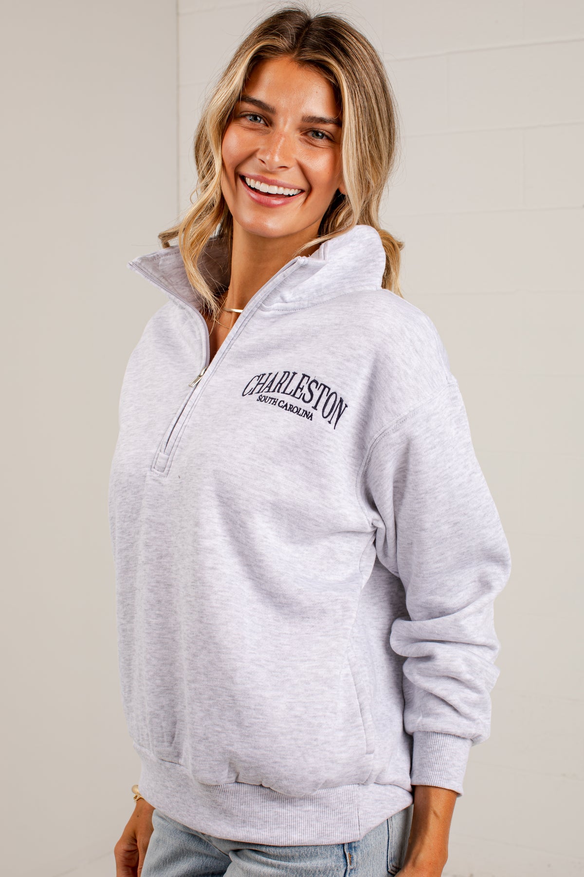A woman wearing a light heather gray quarter-zip hoodie with &