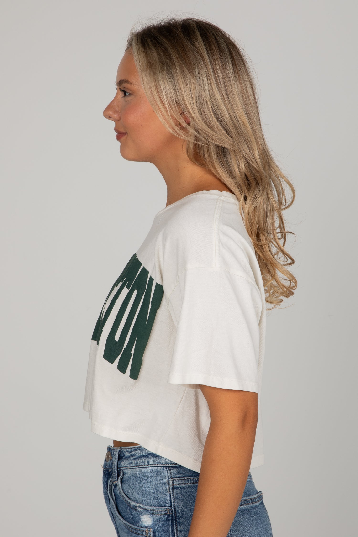 Woman wearing a white t-shirt with green text and blue jeans on a plain background