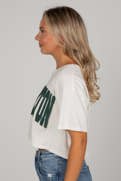 Woman wearing a white t-shirt with green text and blue jeans on a plain background