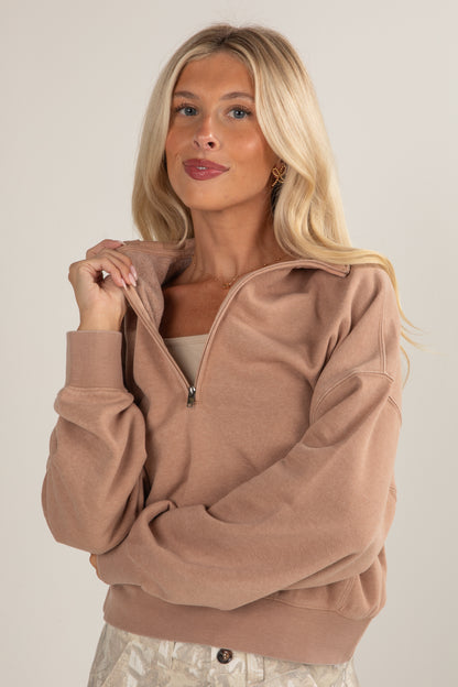 Woman wearing a brown zip-up sweatshirt against a plain background