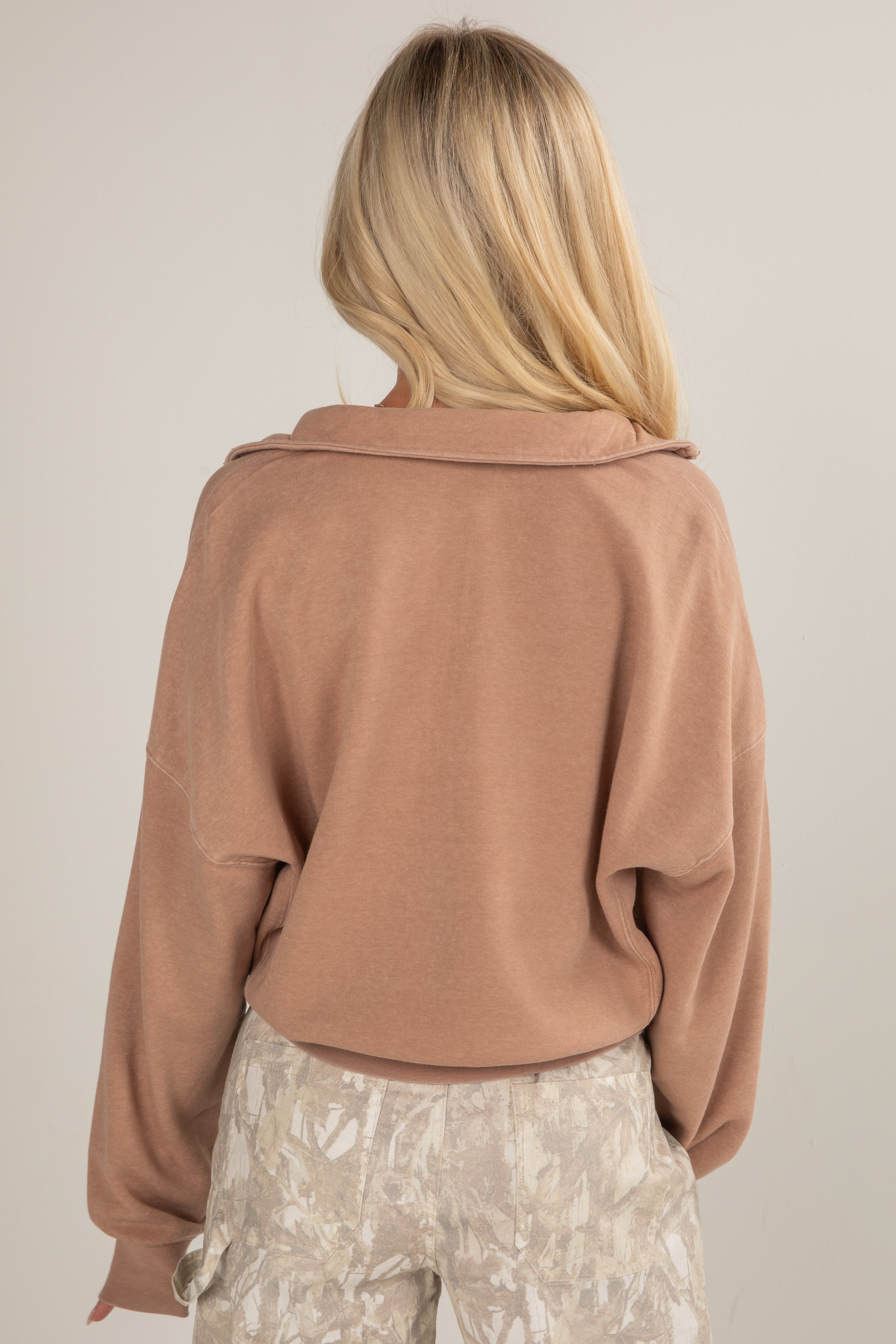 Person wearing a brown sweater and patterned pants against a plain background