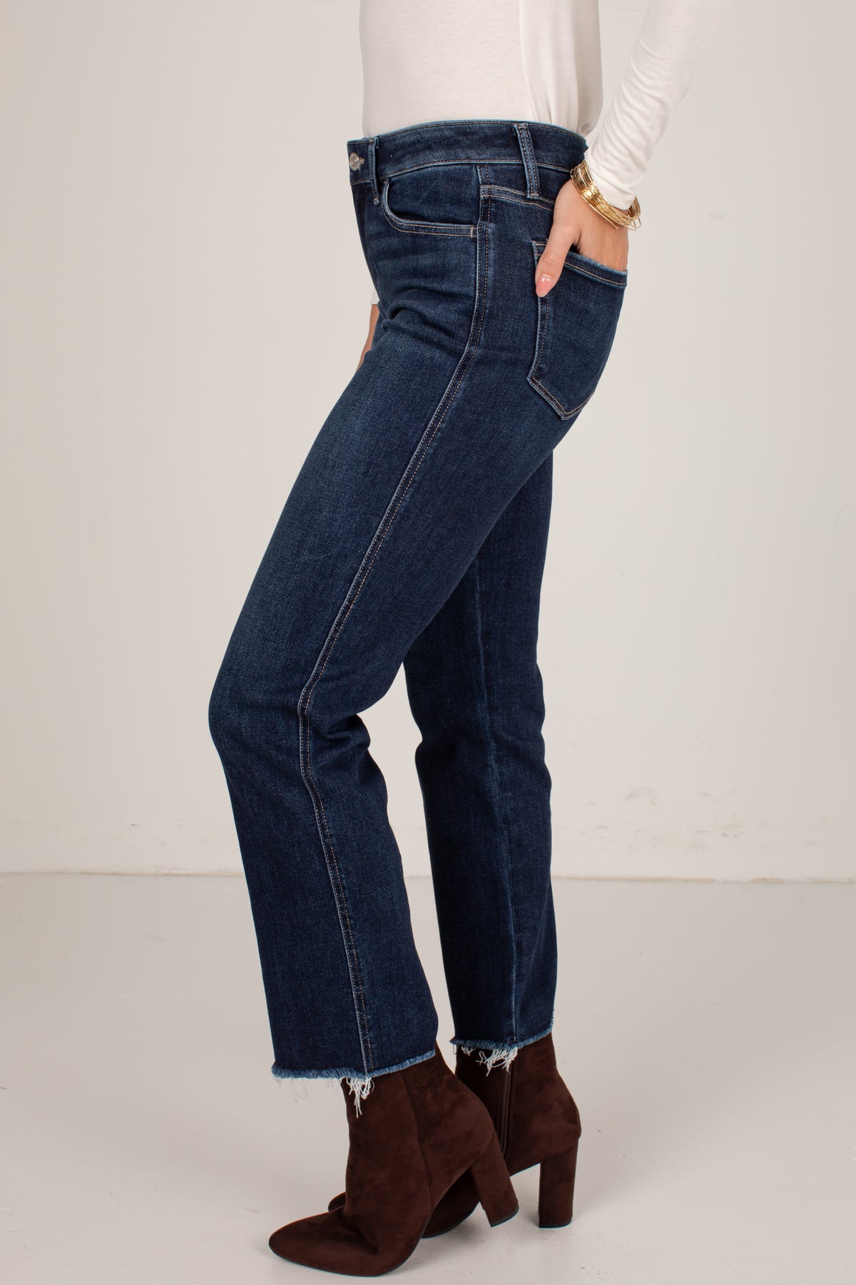 A person wearing dark blue flare jeans with a frayed hem, paired with brown heeled ankle boots and a white long-sleeve top, shown from the waist down against a plain light background.