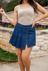 Woman wearing a beige top and blue denim skirt outdoors.