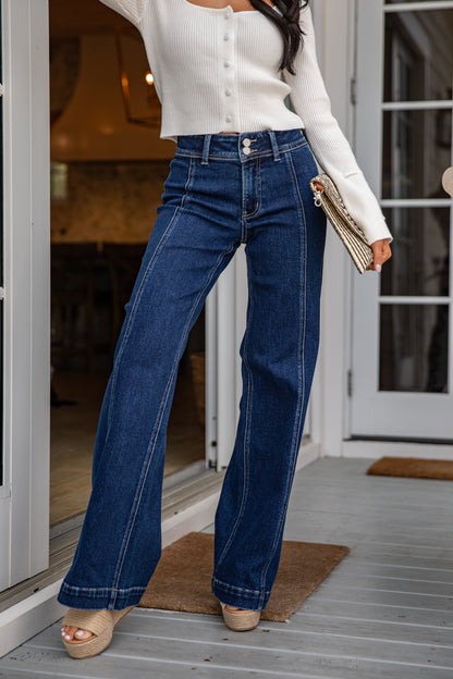 Person wearing blue jeans and a white top, standing on a porch.