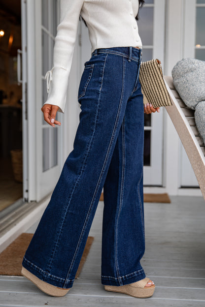 Person wearing blue jeans and a white top, standing on a wooden deck.