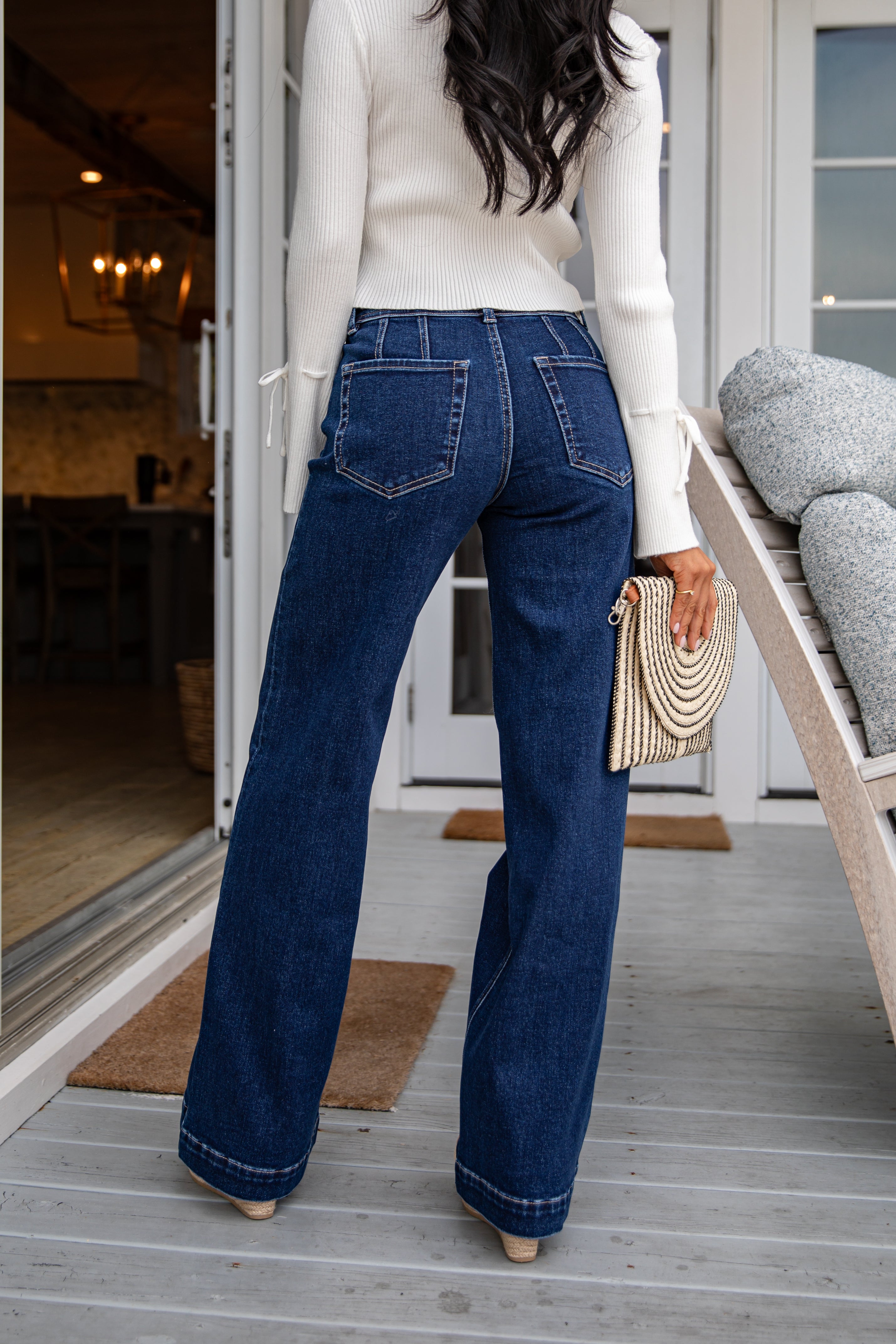 Person wearing blue jeans and a white sweater standing on a wooden deck.