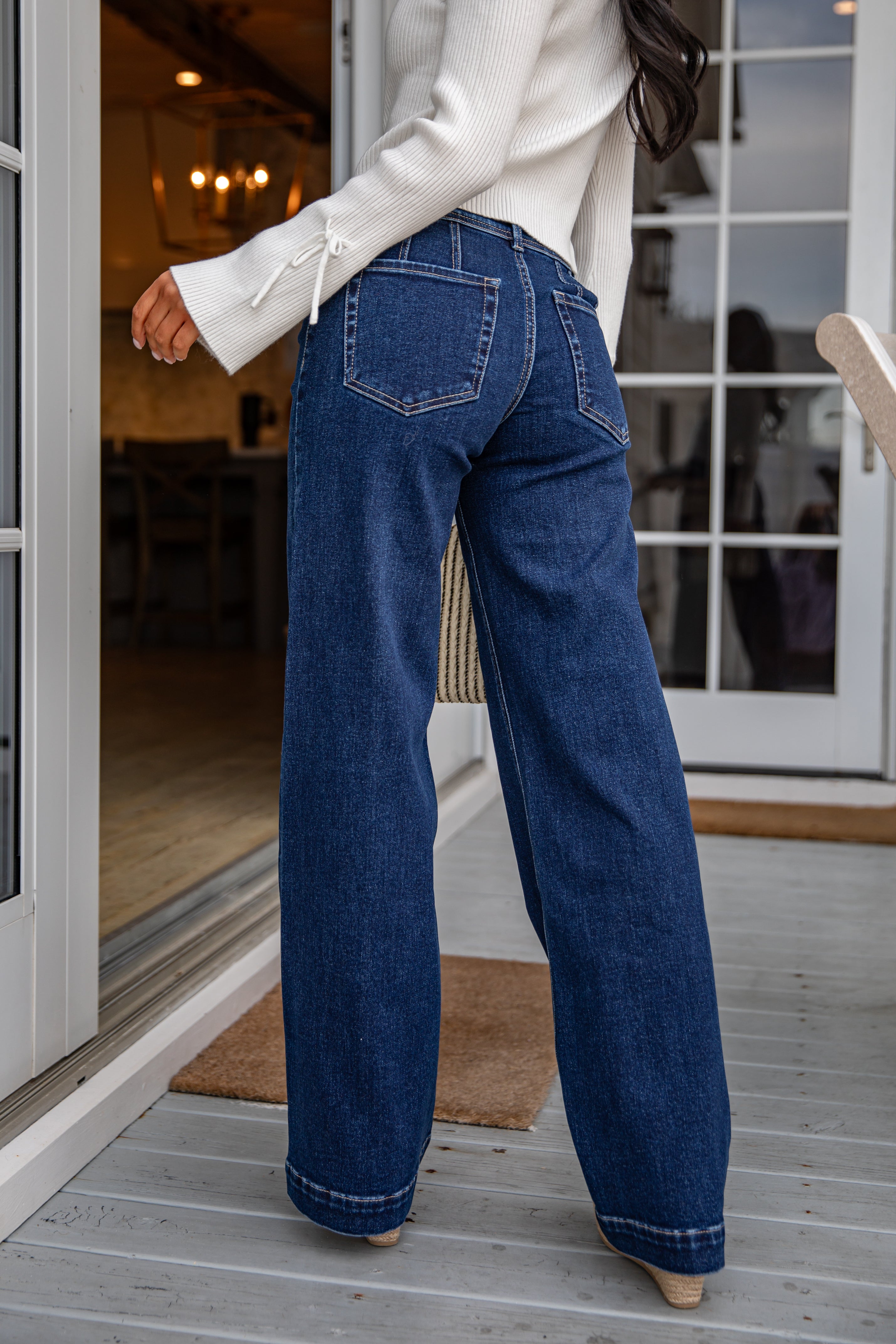 Person wearing blue jeans standing on a wooden deck.