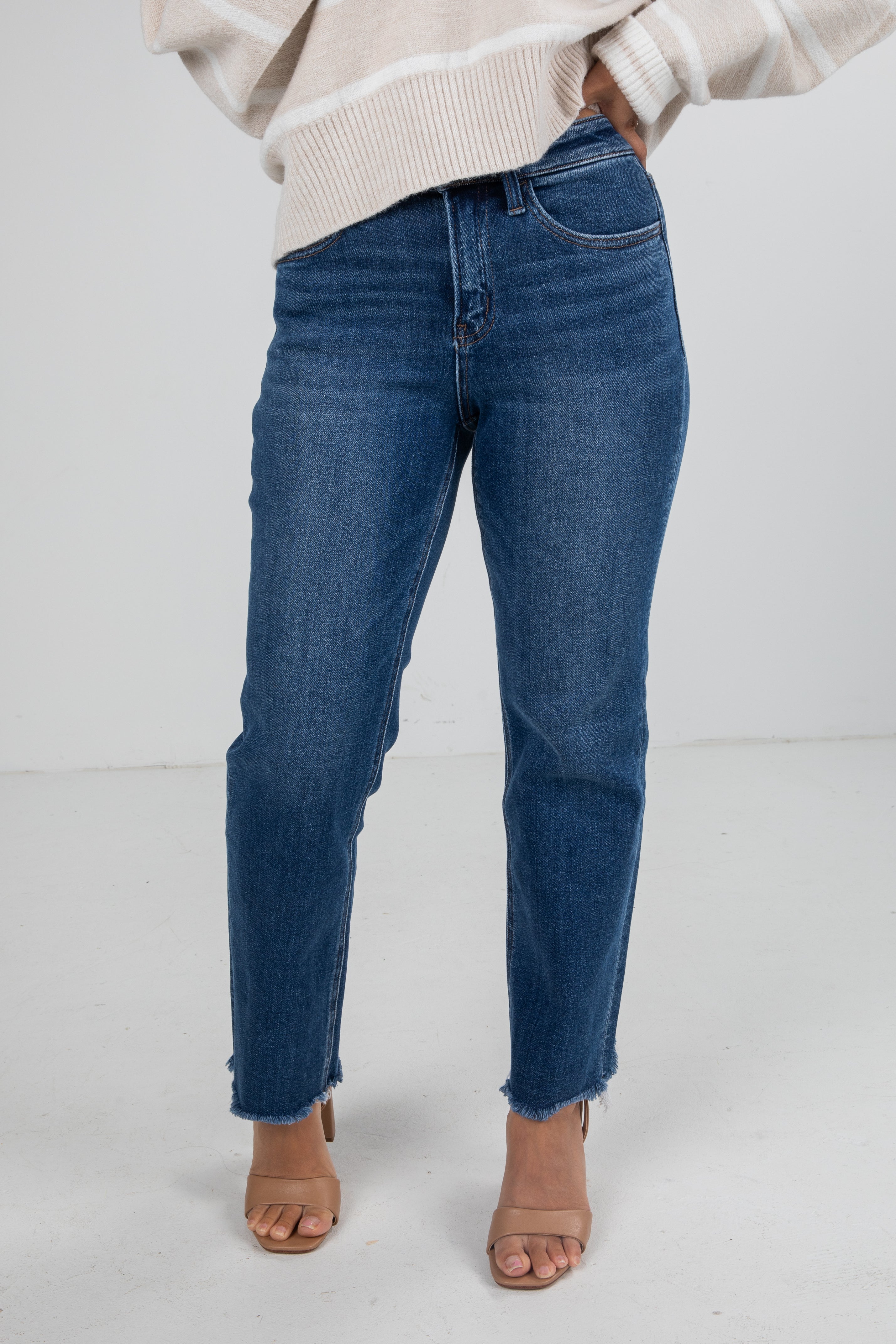 Person wearing blue jeans and a beige sweater on a white background