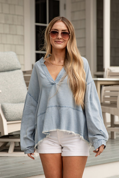 Woman wearing a light blue denim top and white shorts outdoors.