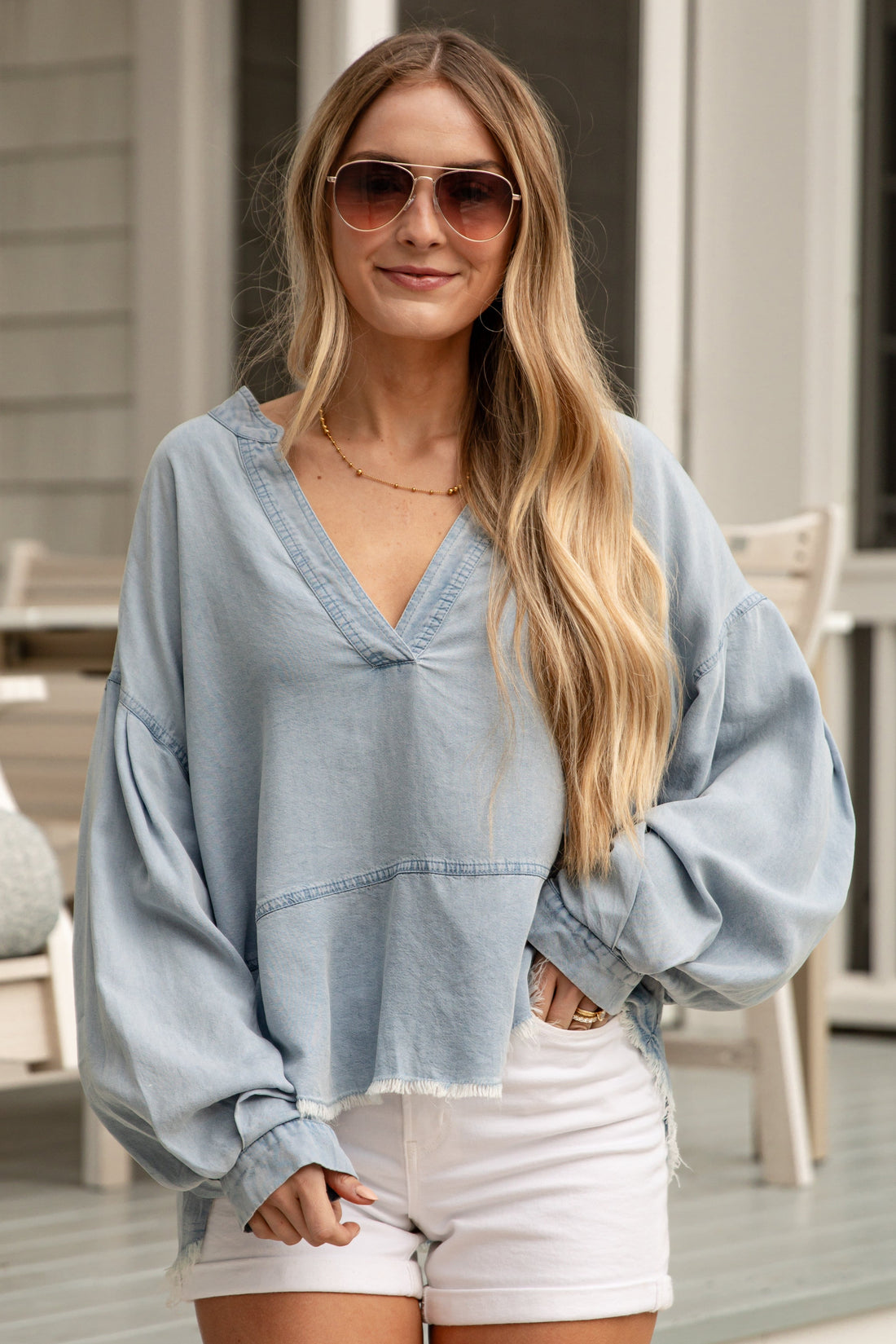 Woman wearing a light blue oversized shirt and white shorts on a porch.