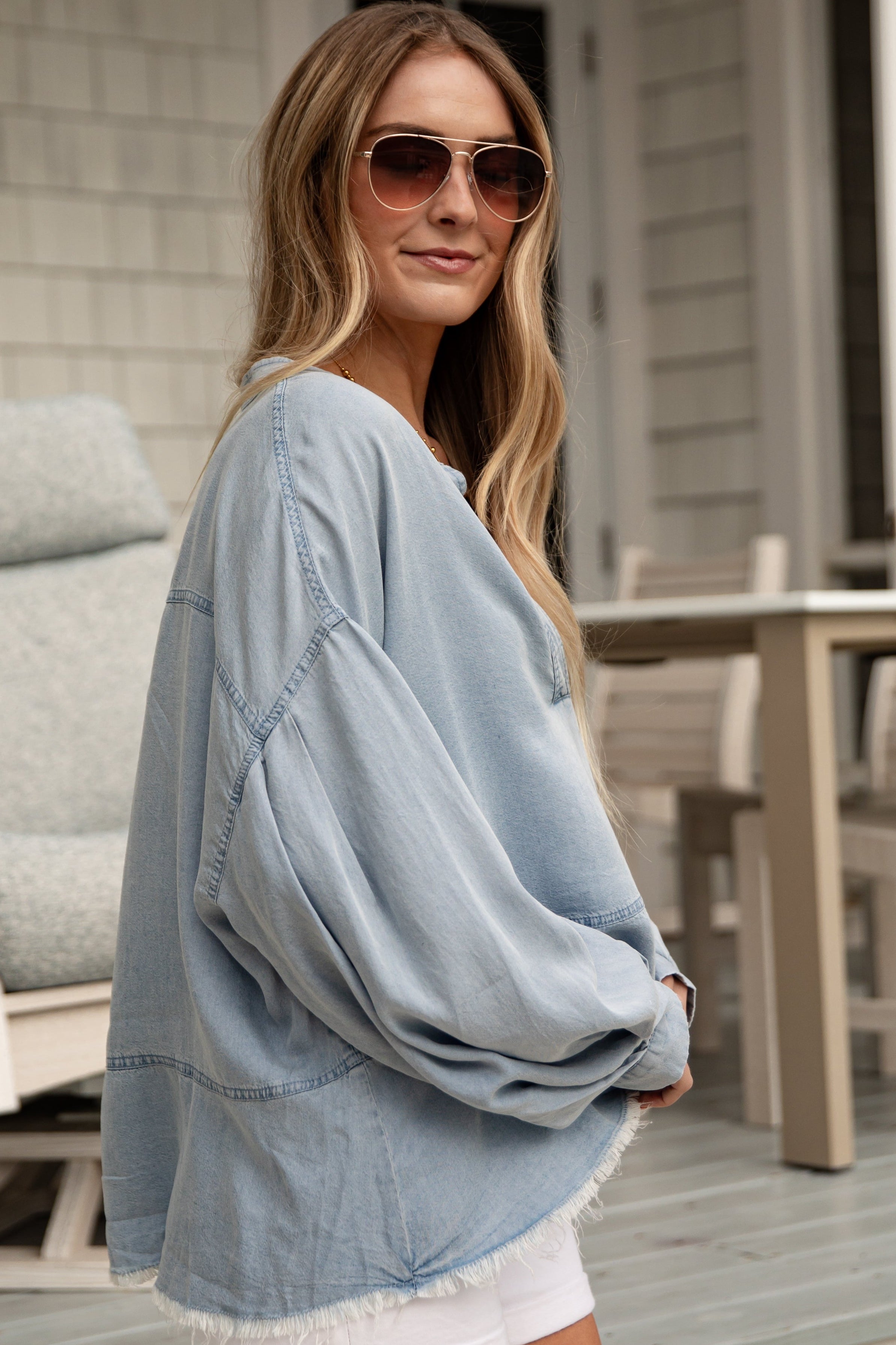 Woman wearing a light blue denim jacket and sunglasses on a porch.