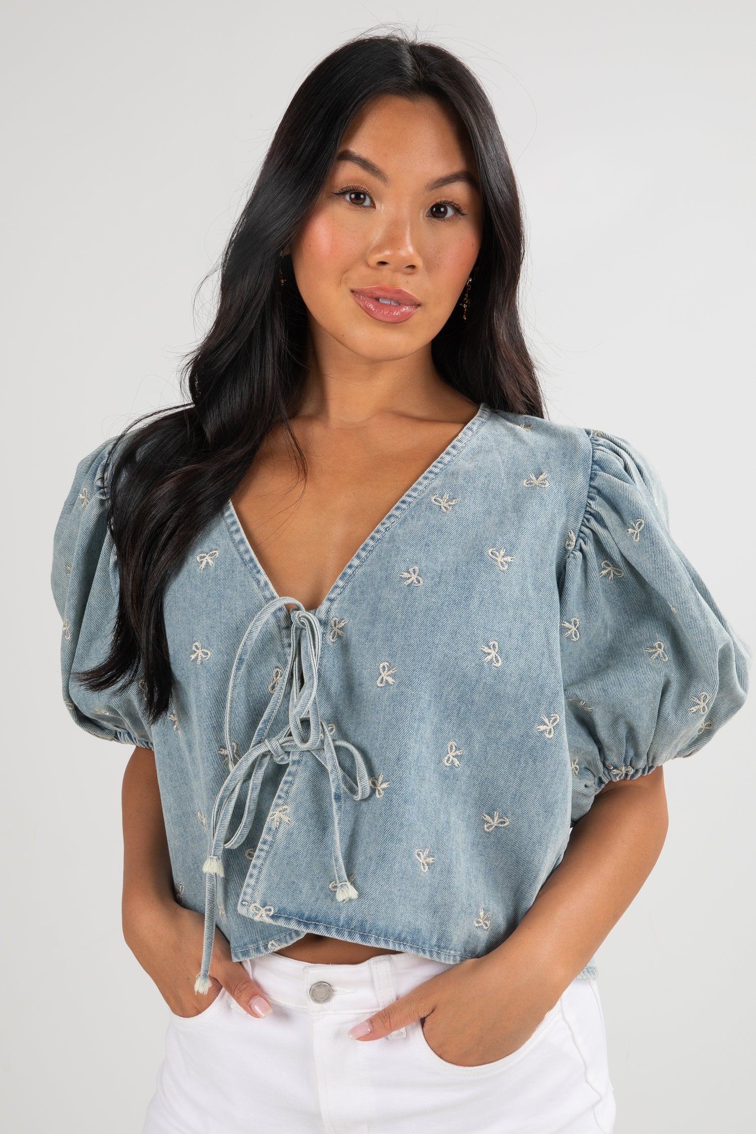 Woman wearing a light blue denim top with embroidered details on a white background