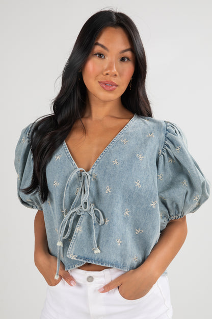 Woman wearing a light blue denim top with embroidered details on a white background