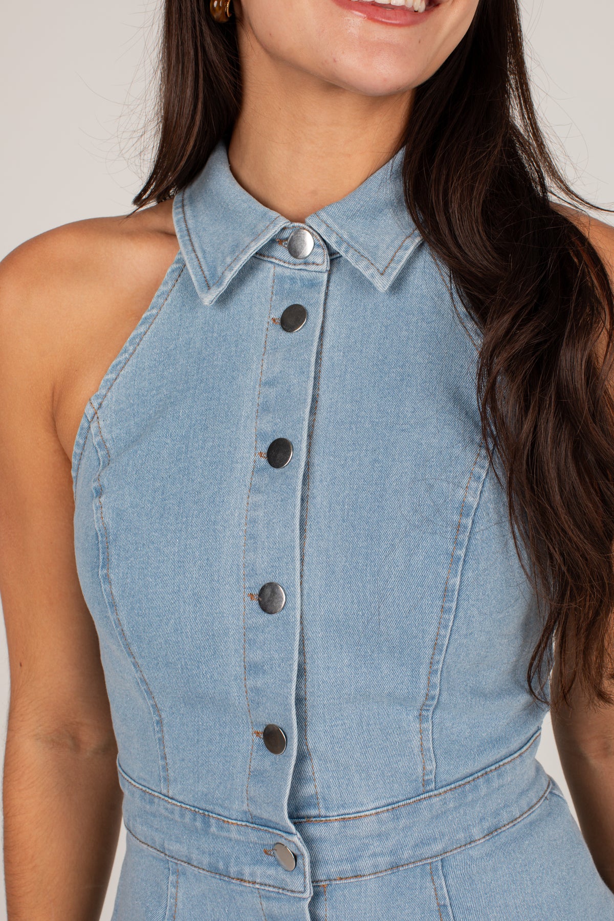 A close-up of a model wearing a light blue denim halter top with a pointed collar and dark buttons down the front.