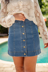 Person wearing a white lace top and blue denim skirt by a pool.
