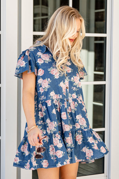 Woman wearing a blue floral dress standing in front of a glass door.