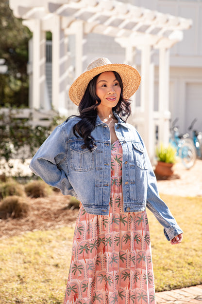 Woman wearing a denim jacket and floral dress with a straw hat outdoors.