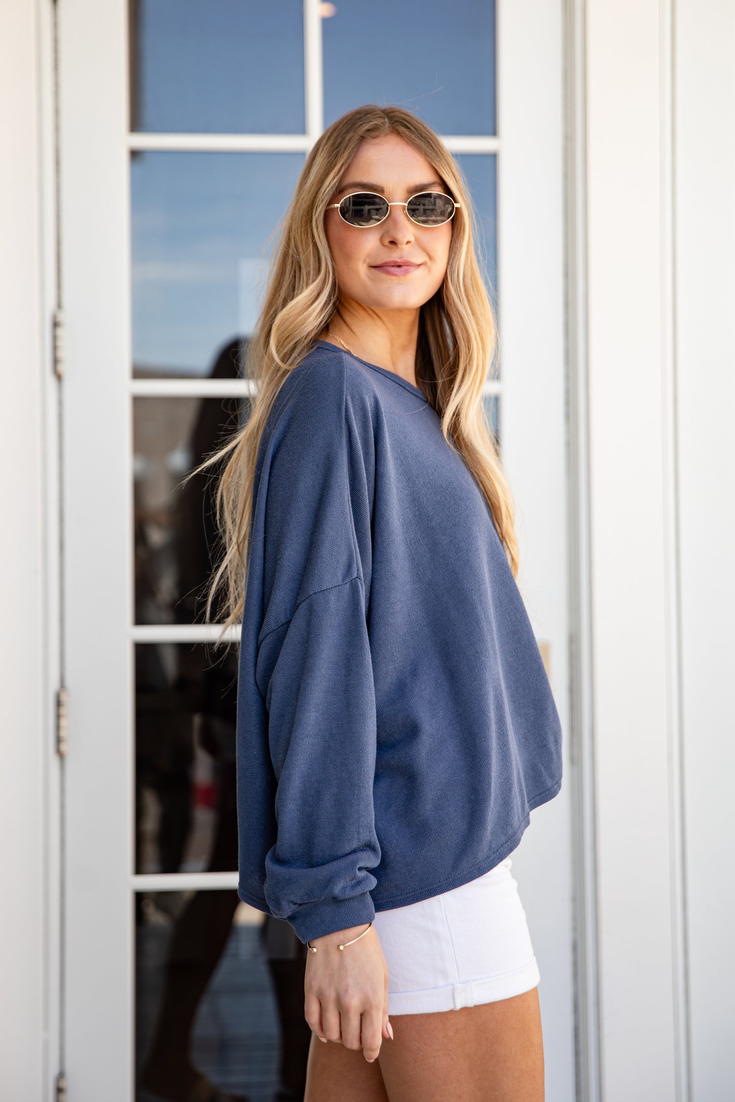 Woman wearing a blue sweatshirt and white shorts standing in front of a glass door.