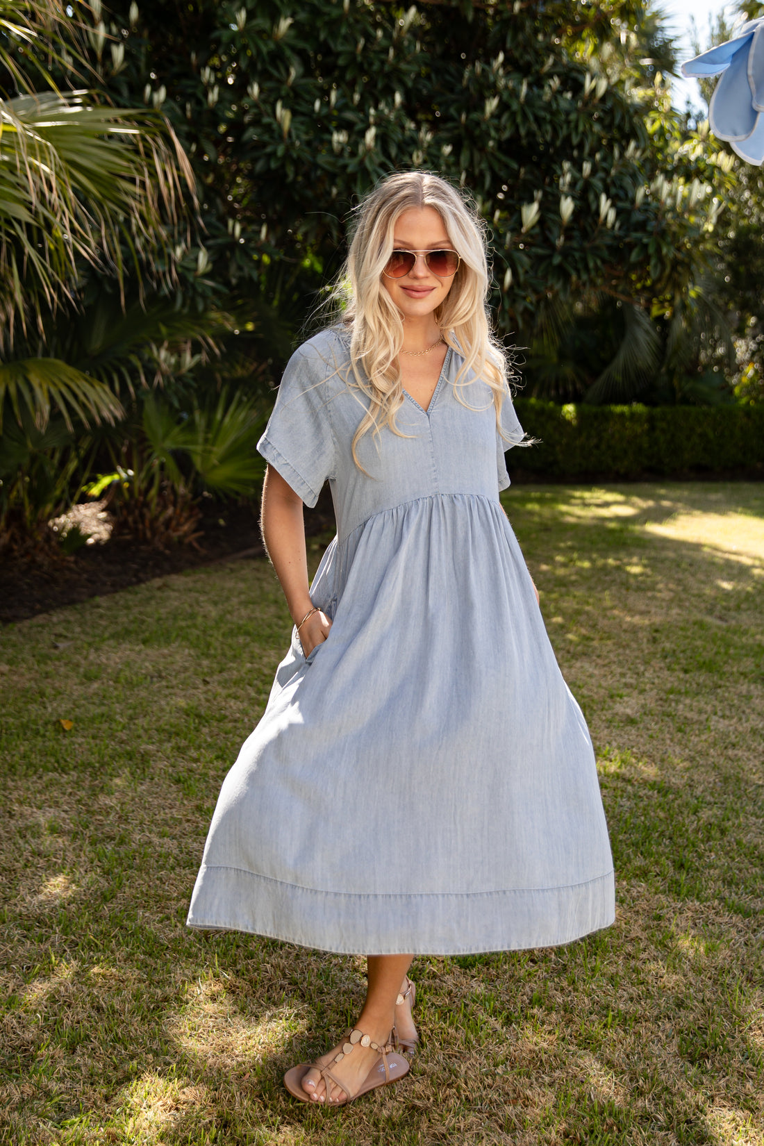 Woman in a light blue dress standing outdoors with greenery in the background